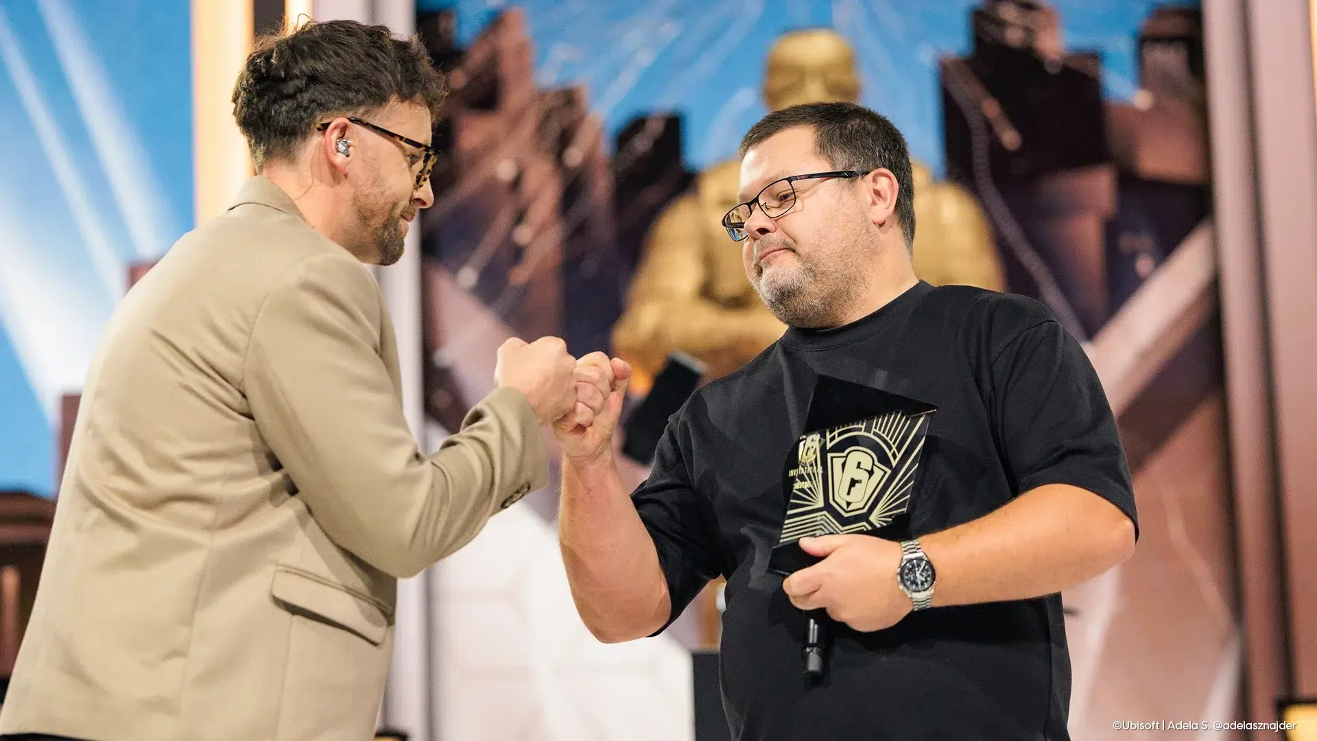 An award handed over on stage, the statue behind
